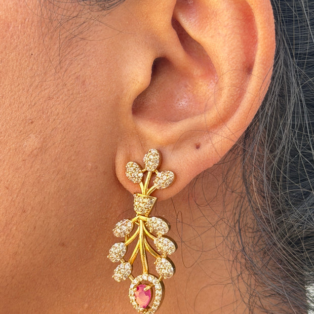 Close-up of an ear wearing a decorative gold earring with a pink gemstone.