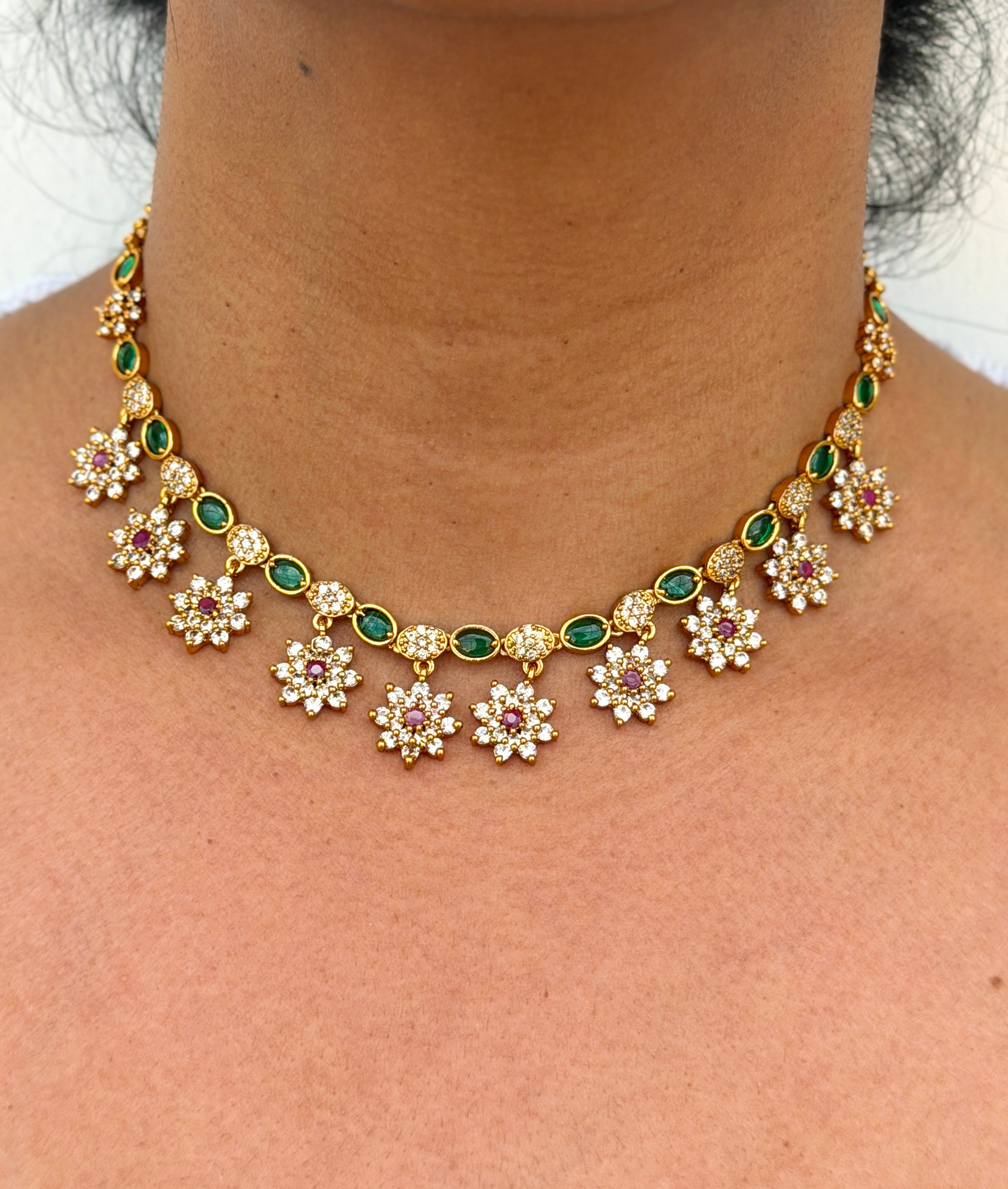 Gold necklace with floral designs and green gemstones 